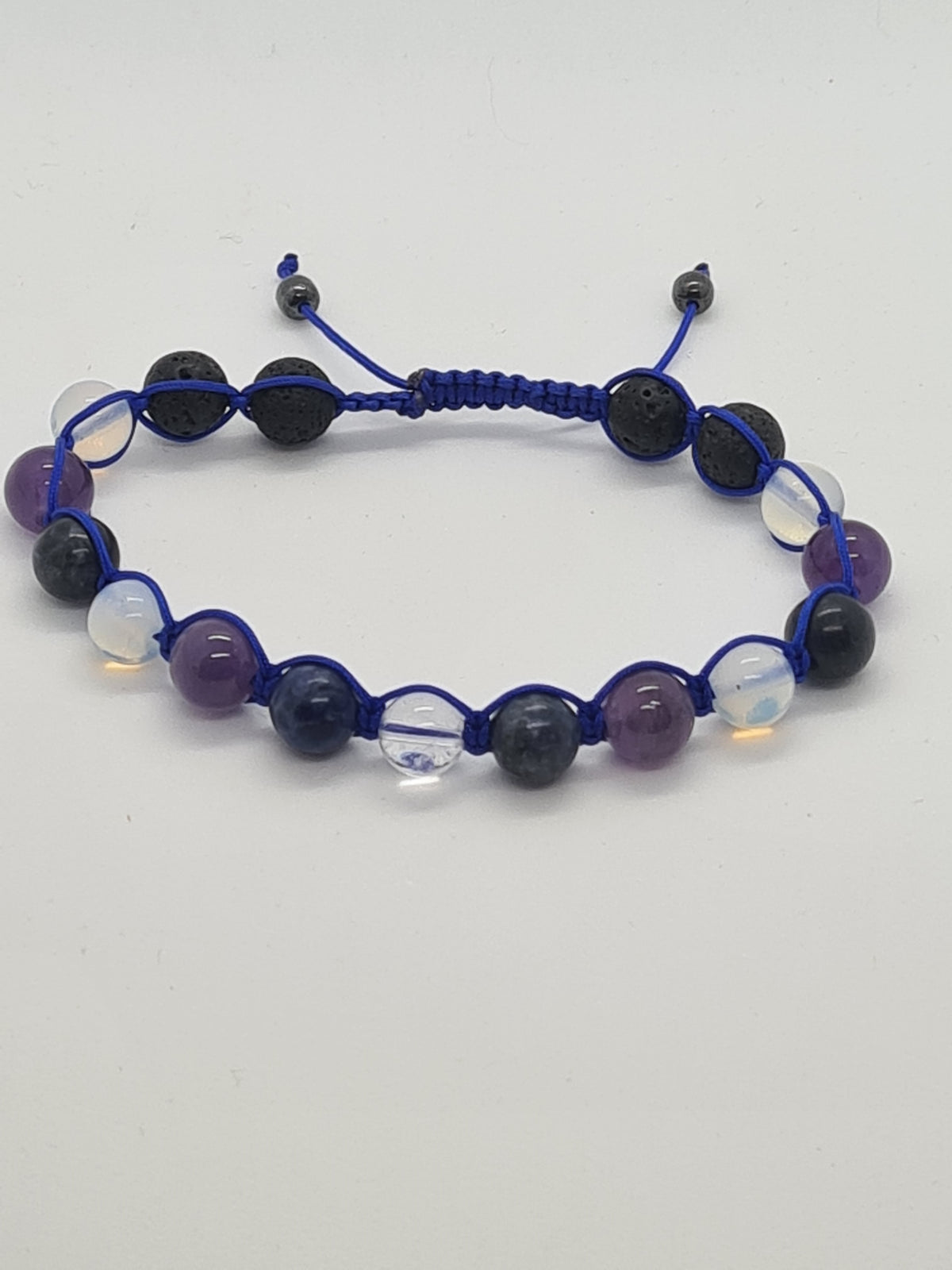 A beaded adjustable cord bracelet featuring purple amethyst, dark black lava stone, clear crystal, and blue cord on a plain white background.